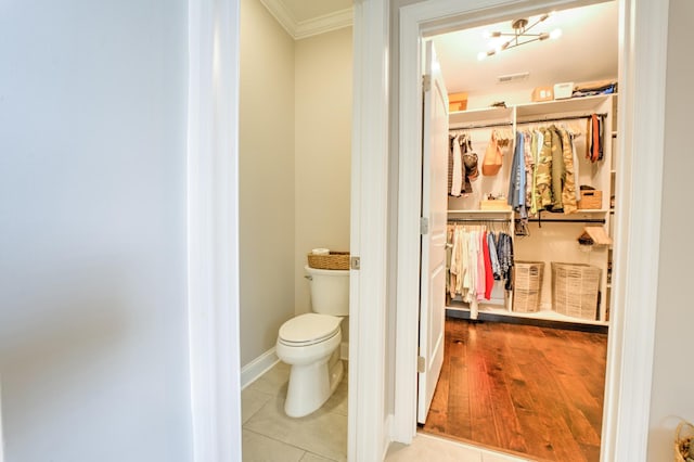 bathroom with toilet, wood finished floors, visible vents, crown molding, and a spacious closet
