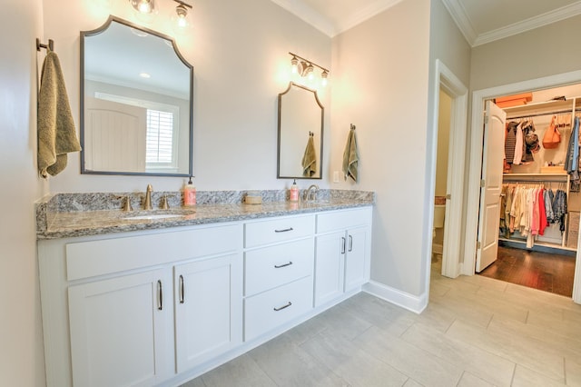 bathroom featuring double vanity, a sink, a walk in closet, crown molding, and baseboards