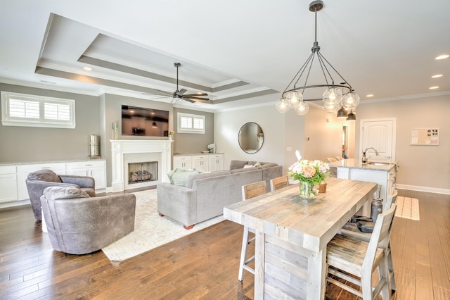 dining area with a ceiling fan, a tray ceiling, crown molding, dark wood-type flooring, and a fireplace