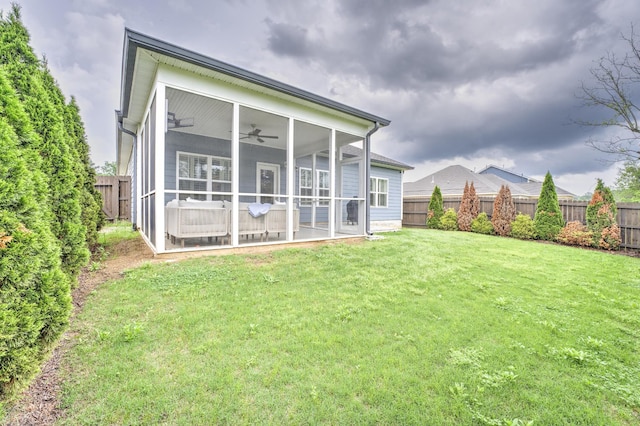 rear view of property featuring a ceiling fan, a sunroom, a fenced backyard, and a lawn
