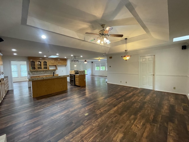 kitchen with open floor plan, an island with sink, ceiling fan, a raised ceiling, and dark wood finished floors