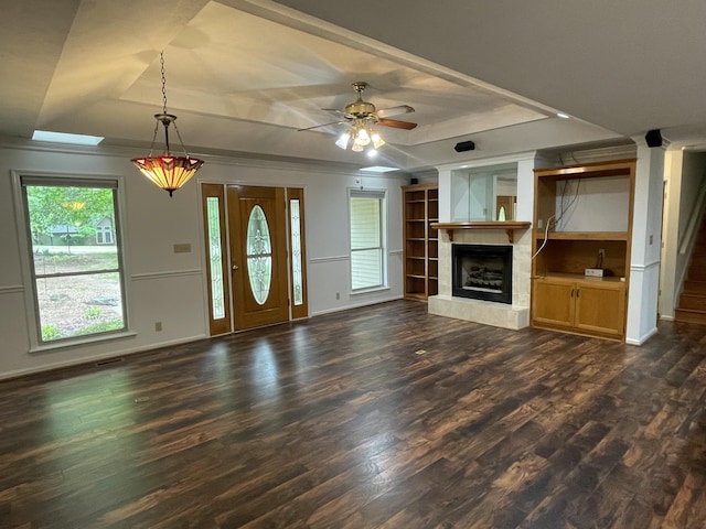 unfurnished living room with a ceiling fan, dark wood finished floors, baseboards, a fireplace with raised hearth, and a tray ceiling