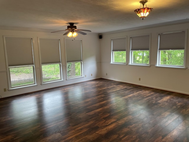 empty room featuring dark wood-type flooring, crown molding, baseboards, and ceiling fan