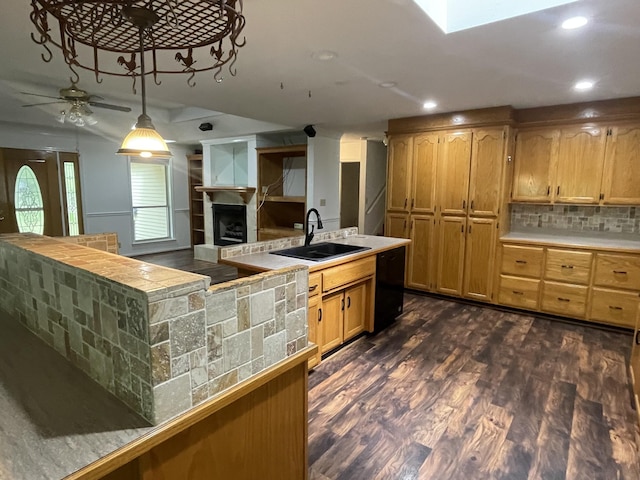 kitchen featuring dark wood-style flooring, ceiling fan, a sink, a tiled fireplace, and decorative backsplash