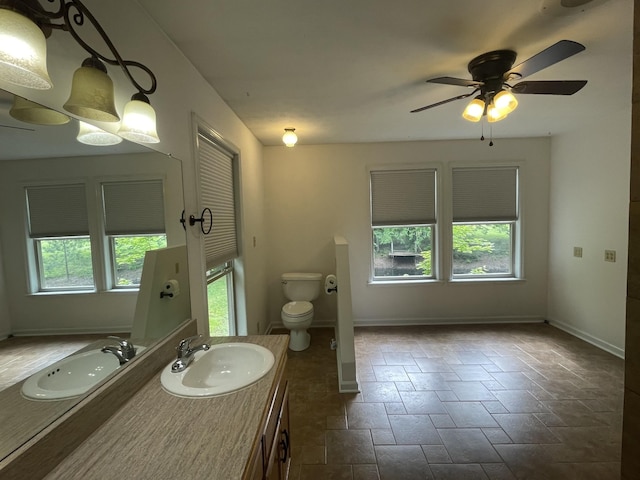 bathroom featuring ceiling fan, vanity, toilet, stone tile floors, and baseboards