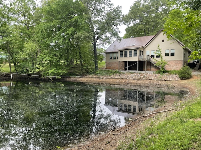 rear view of property featuring a deck with water view, stairs, metal roof, and brick siding