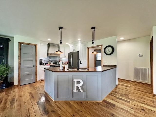 kitchen featuring visible vents, black fridge with ice dispenser, custom exhaust hood, a sink, and light wood-style flooring