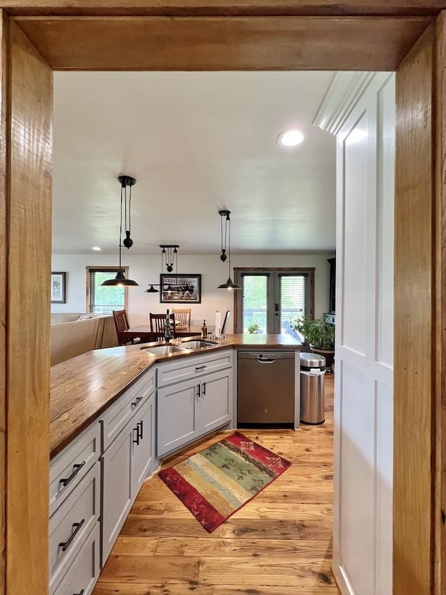 kitchen featuring french doors, a sink, light wood finished floors, dishwasher, and hanging light fixtures
