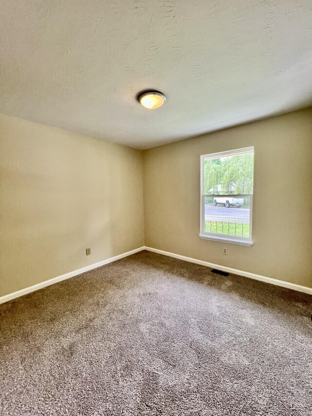 unfurnished room featuring baseboards, carpet flooring, a textured ceiling, and visible vents