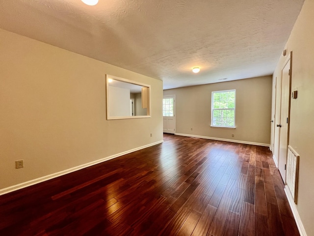 spare room featuring a textured ceiling, baseboards, dark wood finished floors, and visible vents