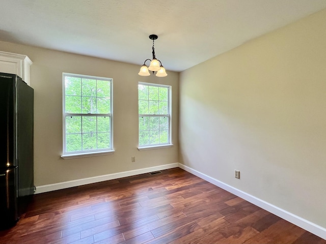 unfurnished dining area featuring baseboards, dark wood finished floors, a chandelier, and visible vents
