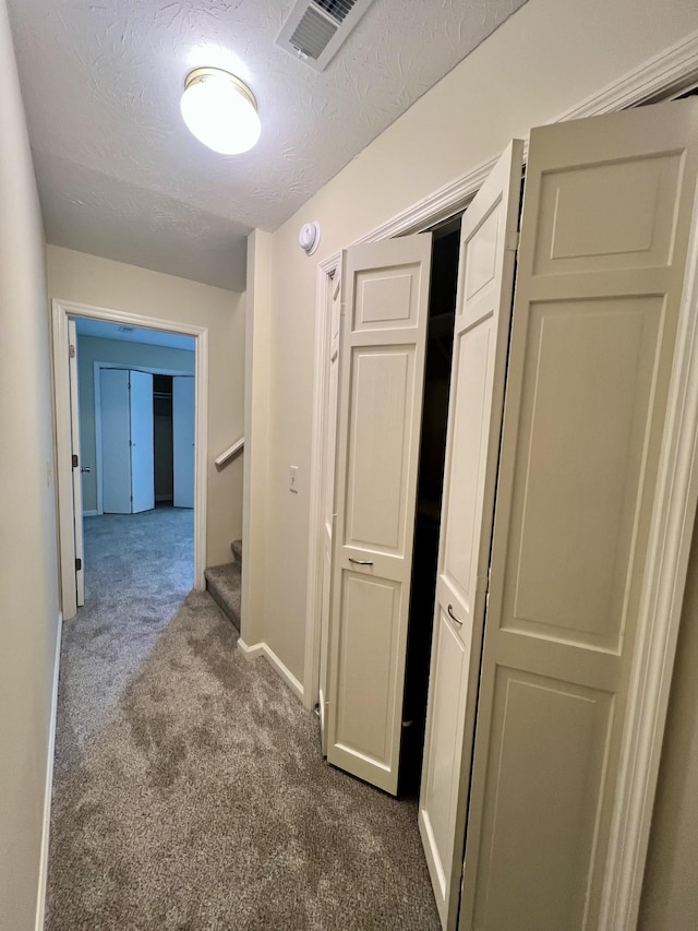 hallway featuring a textured ceiling, dark carpet, stairs, baseboards, and visible vents