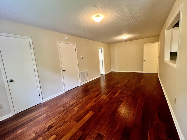 spare room with dark wood-type flooring, a textured ceiling, baseboards, and visible vents