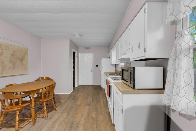 kitchen with baseboards, light countertops, stainless steel microwave, white cabinets, and light wood-style flooring