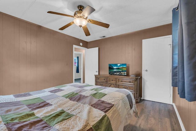 bedroom with wooden walls, dark wood-style flooring, ceiling fan, and visible vents