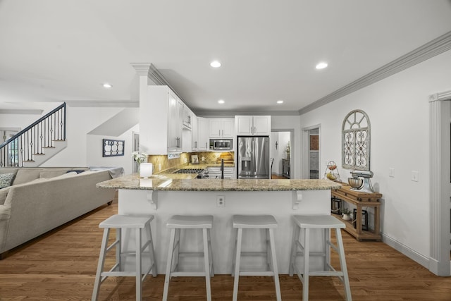 6437 Arno Rd, College Grove, TN 37046 - kitchen featuring appliances with stainless steel finishes, a peninsula, light stone counters, ornamental molding, and a kitchen breakfast bar