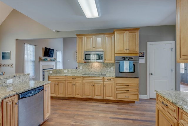 kitchen with decorative backsplash, appliances with stainless steel finishes, a fireplace, light stone countertops, and light wood-style flooring