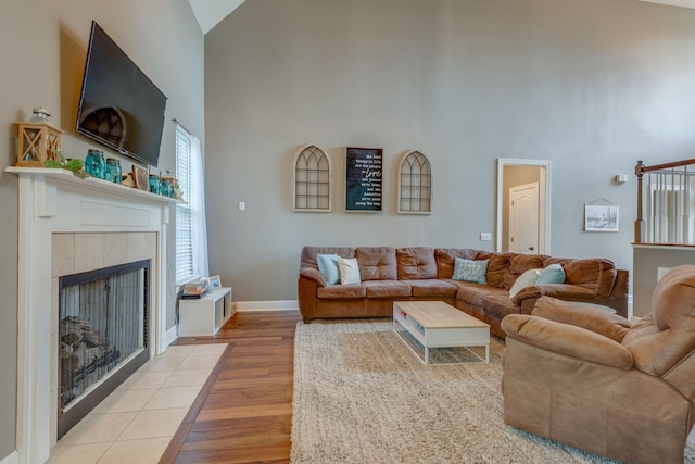 living area with baseboards, high vaulted ceiling, a tiled fireplace, and wood finished floors