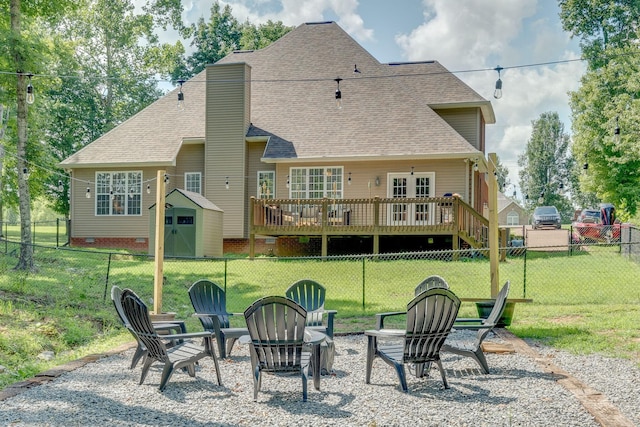 back of property featuring a fire pit, a deck, a fenced backyard, a shingled roof, and a lawn