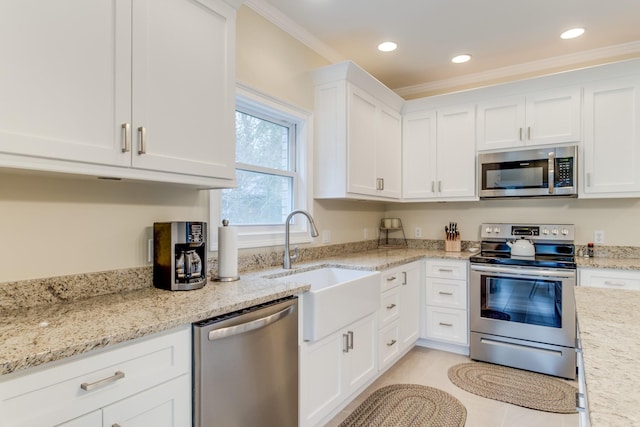 kitchen featuring appliances with stainless steel finishes, light stone countertops, a sink, ornamental molding, and white cabinetry