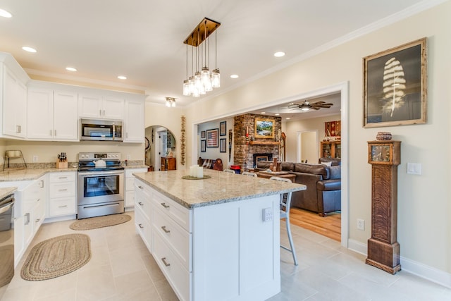 kitchen with appliances with stainless steel finishes, a large fireplace, a center island, light tile patterned floors, and ornamental molding