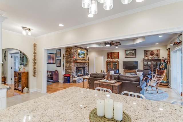 dining room featuring ornamental molding, a fireplace, light wood-type flooring, arched walkways, and a ceiling fan