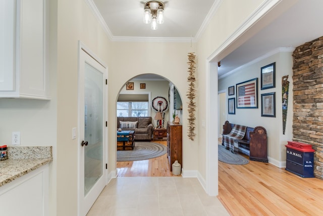 hall with crown molding, arched walkways, baseboards, and light wood finished floors