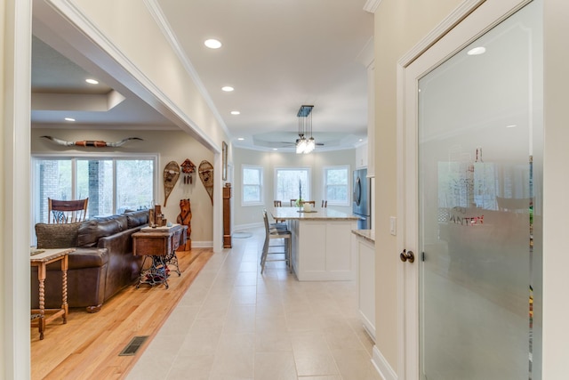 hall featuring crown molding, recessed lighting, a healthy amount of sunlight, and a raised ceiling