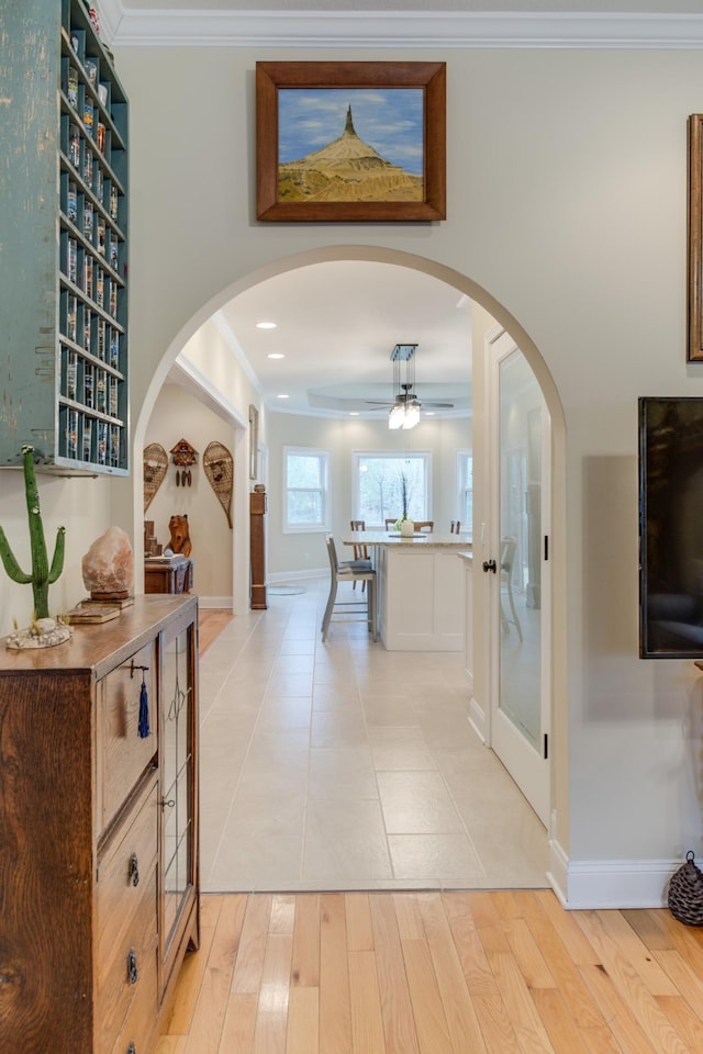 hallway featuring crown molding, arched walkways, light wood-style floors, and baseboards