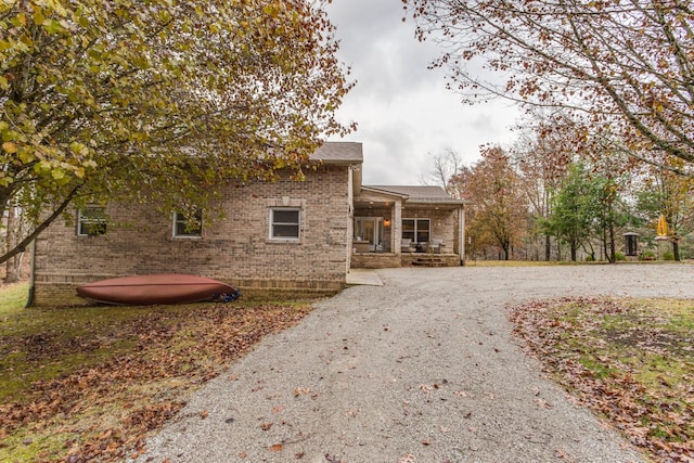 view of front facade with brick siding, gravel driveway, and a porch