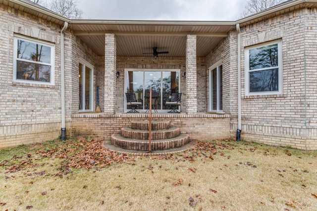 entrance to property featuring brick siding, ceiling fan, and a patio