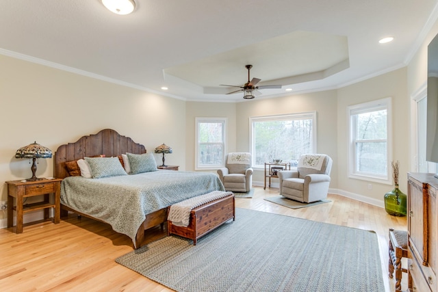 bedroom featuring ceiling fan, ornamental molding, a tray ceiling, and light wood-style flooring