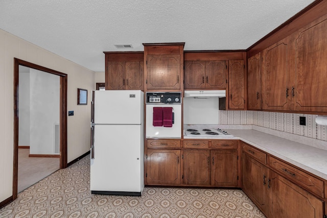 kitchen featuring white appliances, light countertops, a textured ceiling, under cabinet range hood, and brown cabinets