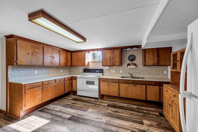 kitchen featuring a sink, brown cabinets, dark wood-style floors, and white appliances