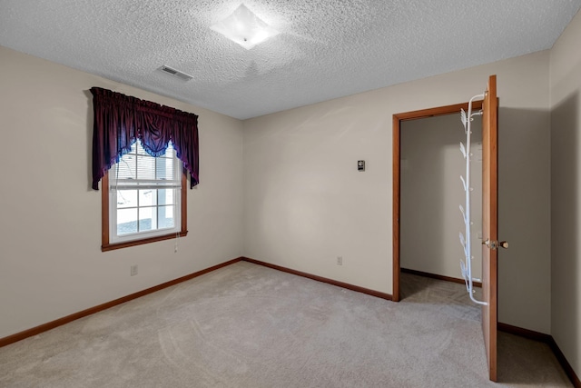 unfurnished room with baseboards, light carpet, a textured ceiling, and visible vents