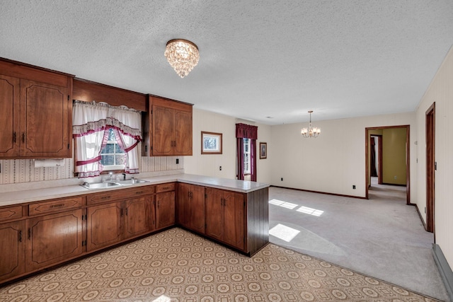 kitchen with a sink, a peninsula, a notable chandelier, and light countertops