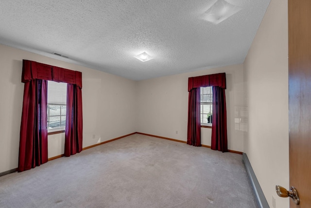 empty room with a textured ceiling, light colored carpet, baseboards, and visible vents