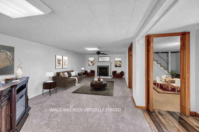 carpeted living room with baseboards, a fireplace with raised hearth, stairs, and wood finished floors