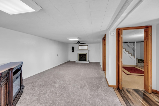 unfurnished living room with carpet, baseboards, a fireplace with raised hearth, and stairs