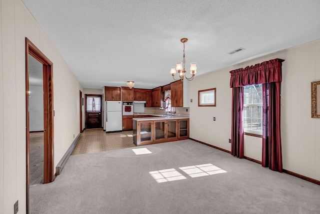 kitchen with light colored carpet, light countertops, a peninsula, a notable chandelier, and white appliances