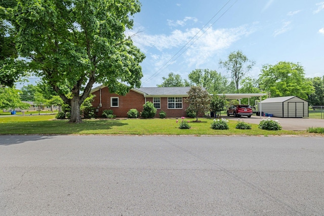 ranch-style house featuring brick siding, a storage shed, an attached carport, a front yard, and an outbuilding
