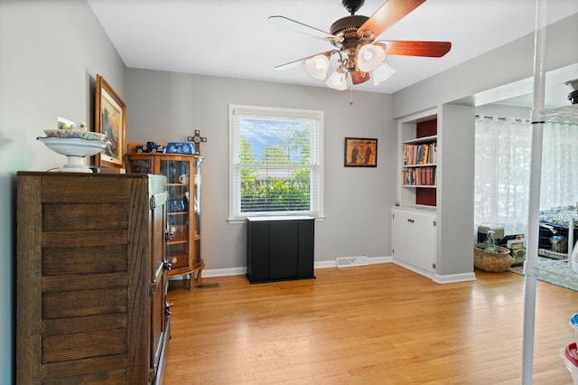 office space featuring visible vents, built in features, baseboards, ceiling fan, and light wood finished floors