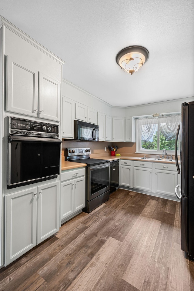 kitchen with light countertops, black appliances, wood finished floors, and white cabinetry