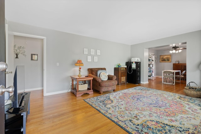 living area with light wood-style floors, baseboards, and a ceiling fan
