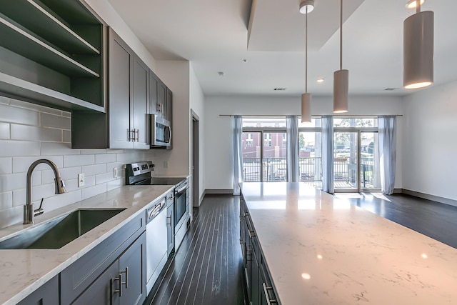 kitchen featuring light stone countertops, baseboards, a sink, dark wood finished floors, and appliances with stainless steel finishes