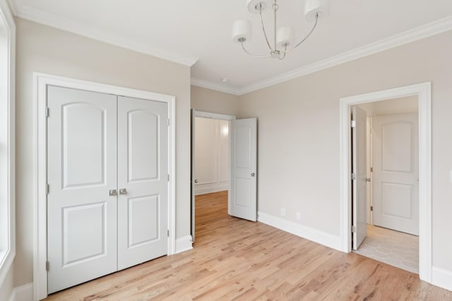 unfurnished bedroom with crown molding, baseboards, a closet, a notable chandelier, and light wood-style floors