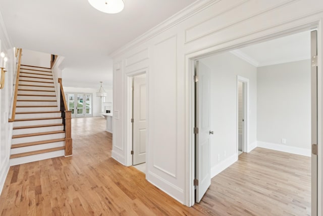 hall featuring light wood-style floors, stairs, crown molding, and baseboards