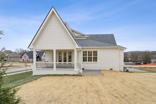 rear view of property featuring covered porch, crawl space, french doors, roof with shingles, and brick siding