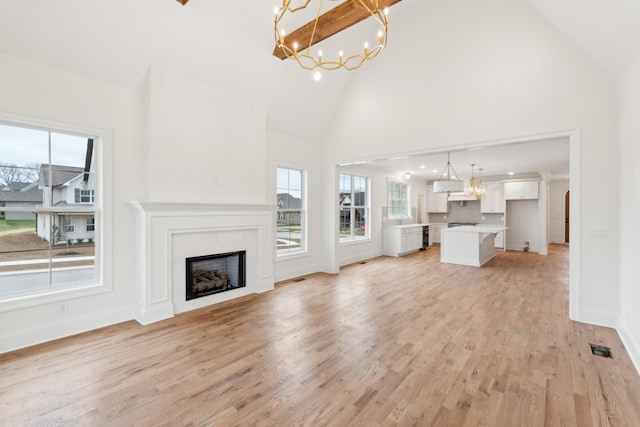 unfurnished living room featuring high vaulted ceiling, a fireplace, light wood-type flooring, and a notable chandelier