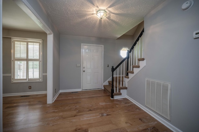 foyer with stairway, baseboards, wood-type flooring, and visible vents
